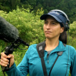 woman outdoors wearing headphones and holding a microphone